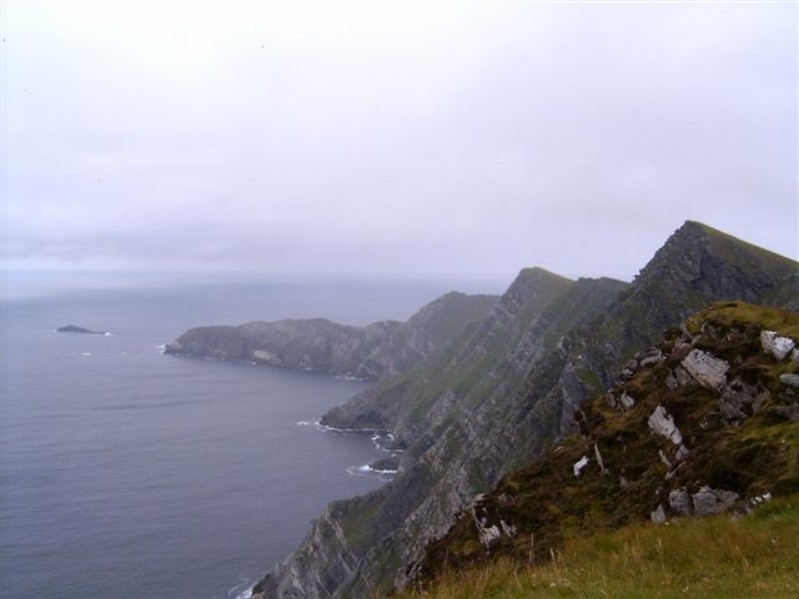 widok irnaldzkiego wybrzeża- fragmen zielonej łąki, szare skały i morze, dookoła unosi się mgła