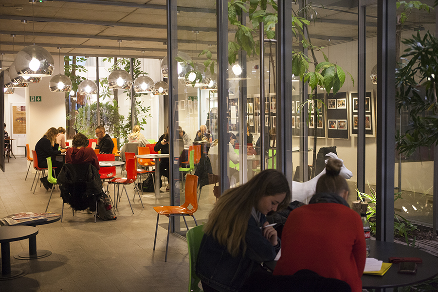 zdjęcie przedstawia Herbaciarnię, jasną przestrzeń ze siedzącymi przy kolorowych stolikach ludżmi