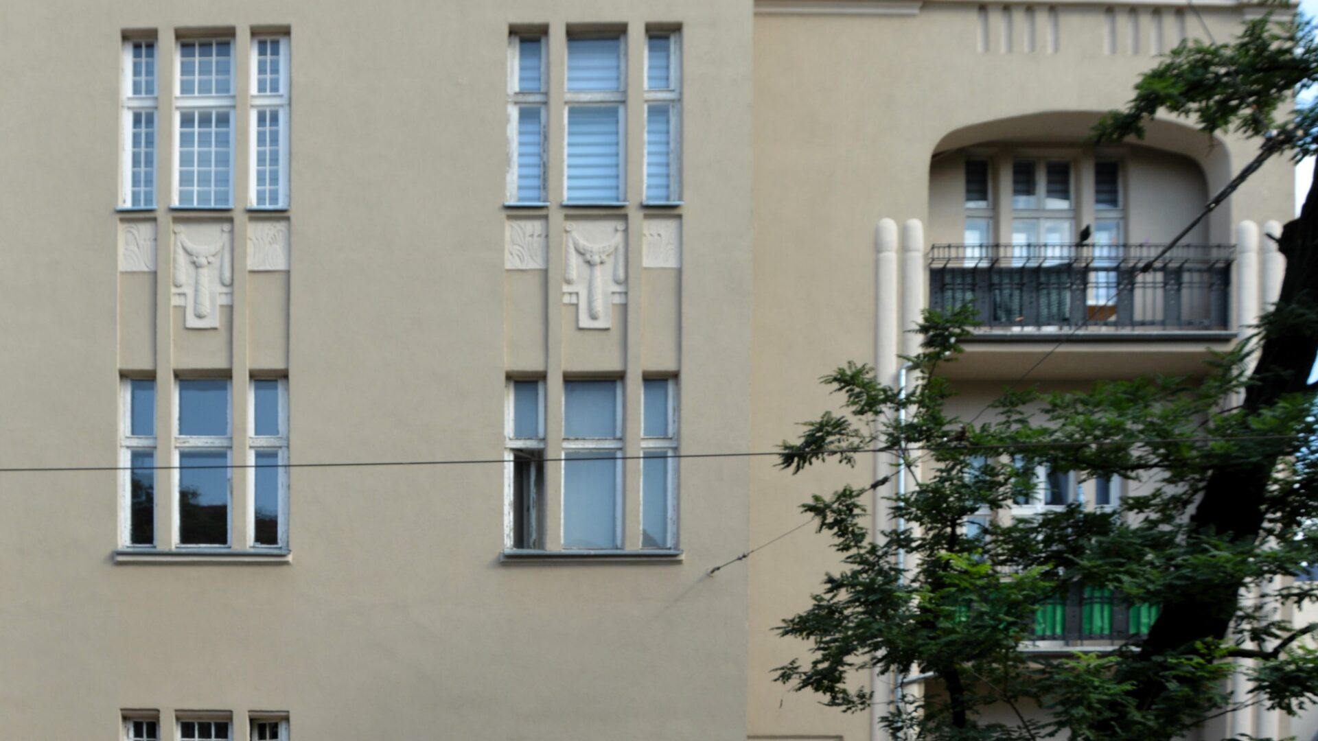 Obrazek do oprowadzania po mieszkaniu Kazimiery Iłłakowiczówny. Na fotografii kamienica, w której mieszkała poetka, łukowe wejście, po prawej stronie lodżie i drzewo.