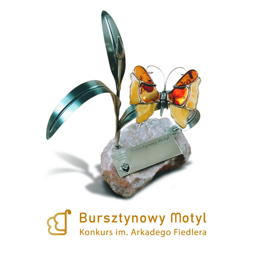 Obrazek do wydarzenia, fotografia statuetki nagrody Bursztynowego Motyla. Na kamieniu metalowa łodyga rośliny, na której przysiadł motyl wykonany z bursztynu, obok tabliczka z nazwą nagrody i firmą Ania Kruk.