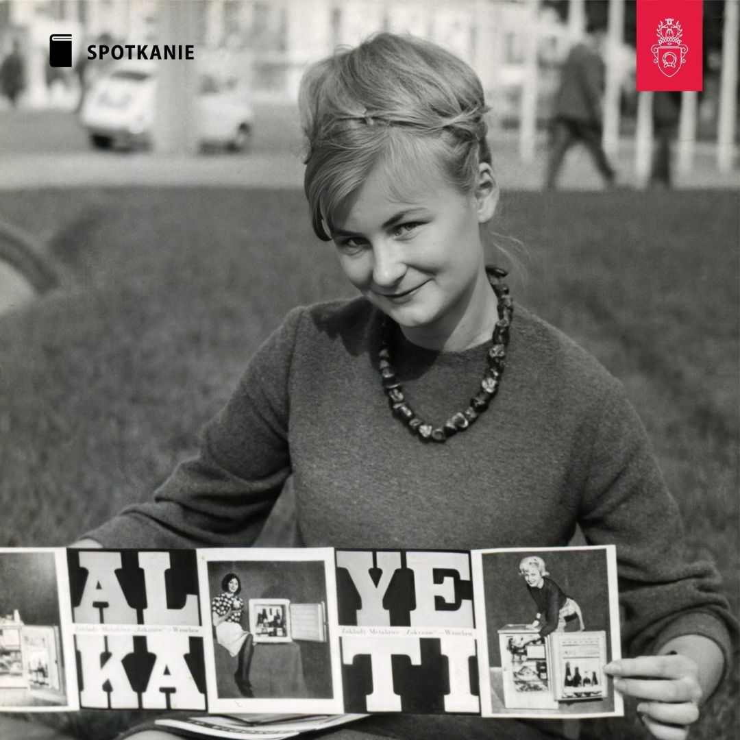 Obrazek do wydarzenia, czarno-biała fotografia, uśmiechnięta kobieta w koku z blond włosów, swetrze i koralach prezentuje katalog zakładów metalowych. Fotografia z lat 60.