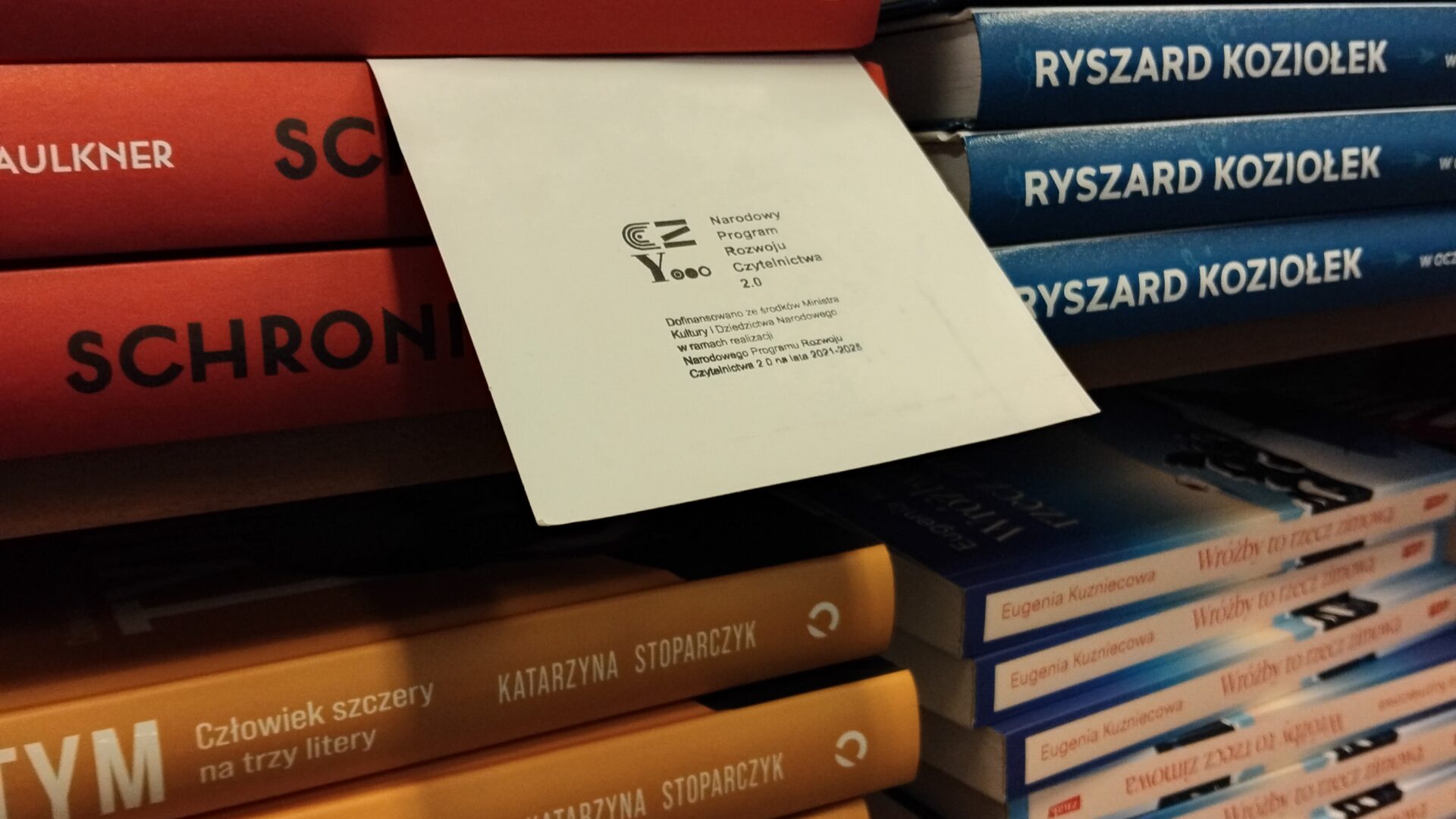 Stos książek z kartką z pieczęcią Narodowego Programu Rozwoju Czytelnictwa 2.0