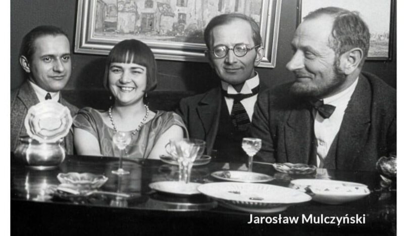 Obrazek do wydarzenia. Okładka książki przedstawia czarno-białą fotografię z dawnych lat. Trzech mężczyzn i kobieta siedzą przy stole, śmieją się. Na stole talerzyki, kieliszki, na ścianie za nimi obrazy.
