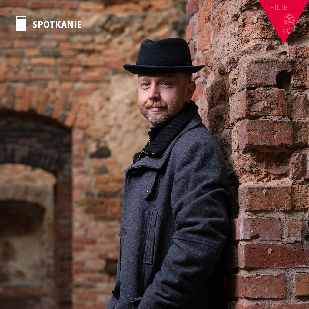 Obrazek do wydarzenia, autor, mężczyzna z zarostem w kapeluszu na tle ceglanego muru.