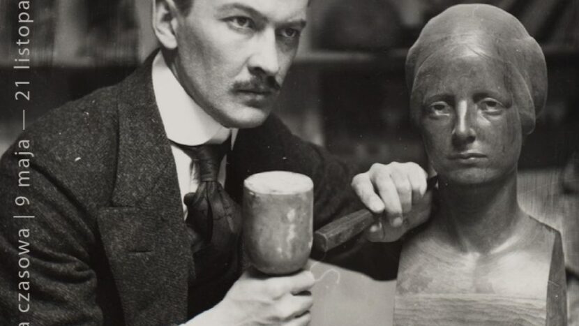 Obrazek do wydarzenia. Czarno biała fotografia artysty - mężczyzna w garniturze, z wąsem, patrzący w dal, trzyma dłuto przy rzeźbie - popiersiu kobiety.