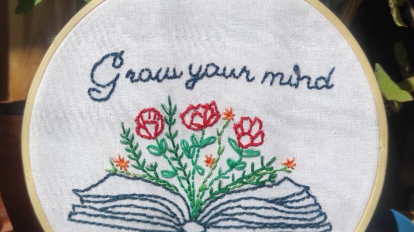 Obrazek do wydarzenia, tamborek z płótnem, wyhaftowanym napisem w języku angielskim "grow your mind" oraz książką, z której wyrastają kwiaty.