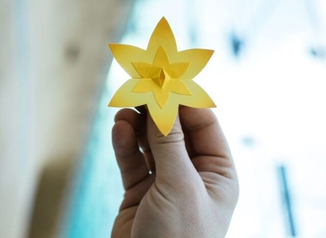 Obrazek do wydarzenia, widać dłoń trzymającą żółtego żonkila zrobionego z papieru