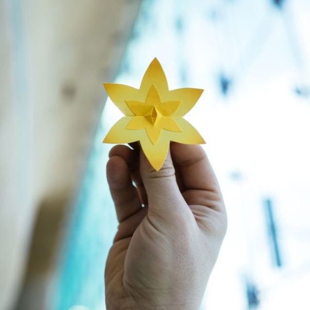 Obrazek do wydarzenia, widać dłoń trzymającą żółtego żonkila zrobionego z papieru