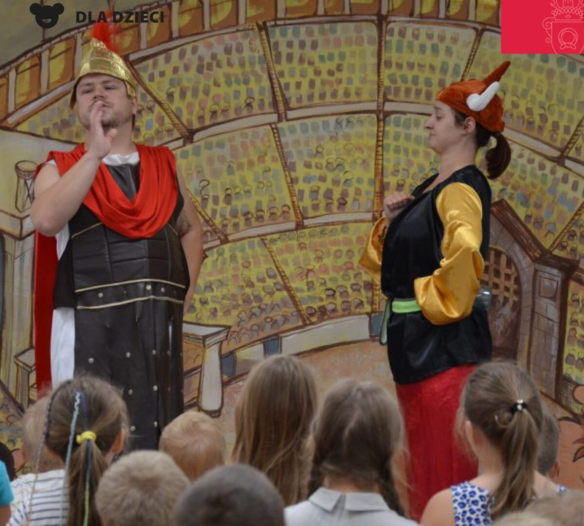Obrazek do wydarzenia. Scenka teatralna, młodzi aktorzy, kobieta i mężczyzna w hełmach galijskim i rzymskim, z przodu młoda widownia.