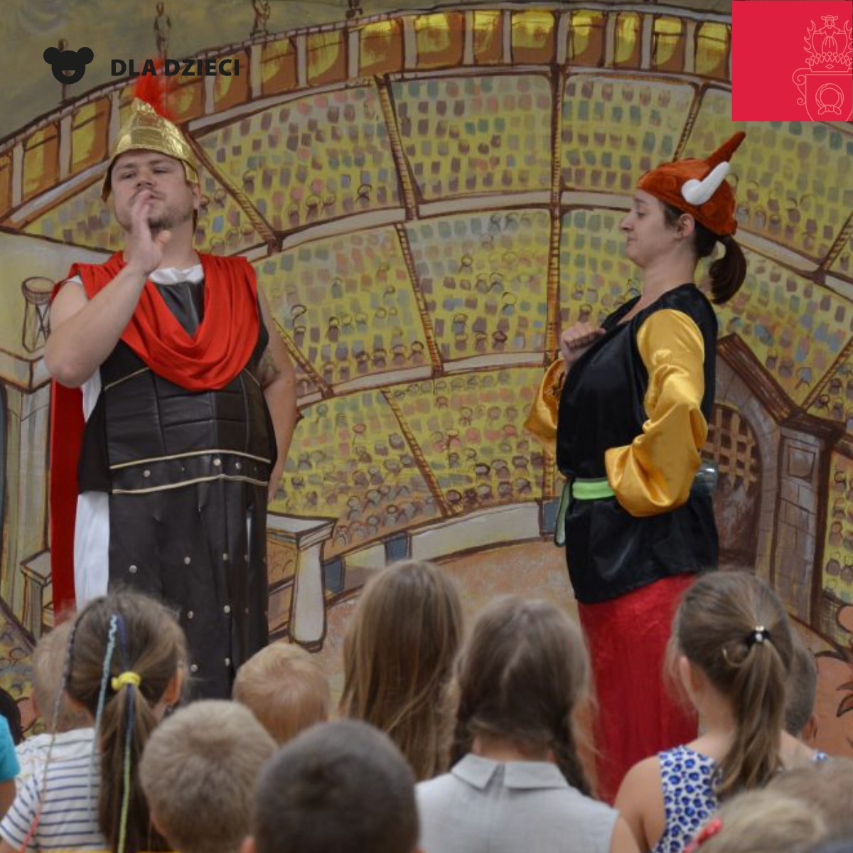 Obrazek do wydarzenia. Scenka teatralna, młodzi aktorzy, kobieta i mężczyzna w hełmach galijskim i rzymskim, z przodu młoda widownia.