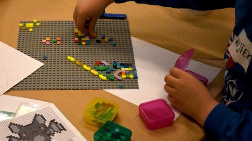 Obrazek do wydarzenia, barwa zdjęcie fragmentu stołu z podkładka do układania i klockami lego oraz dziecięcymi rękami.