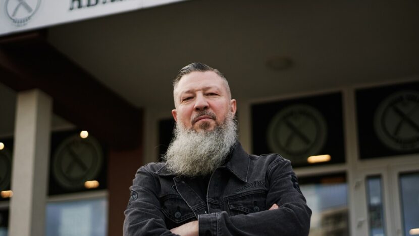 Obrazek do wydarzenia. Na fotografii mężczyzna z długą brodą, nad nim szyld Adam Szulc barber.